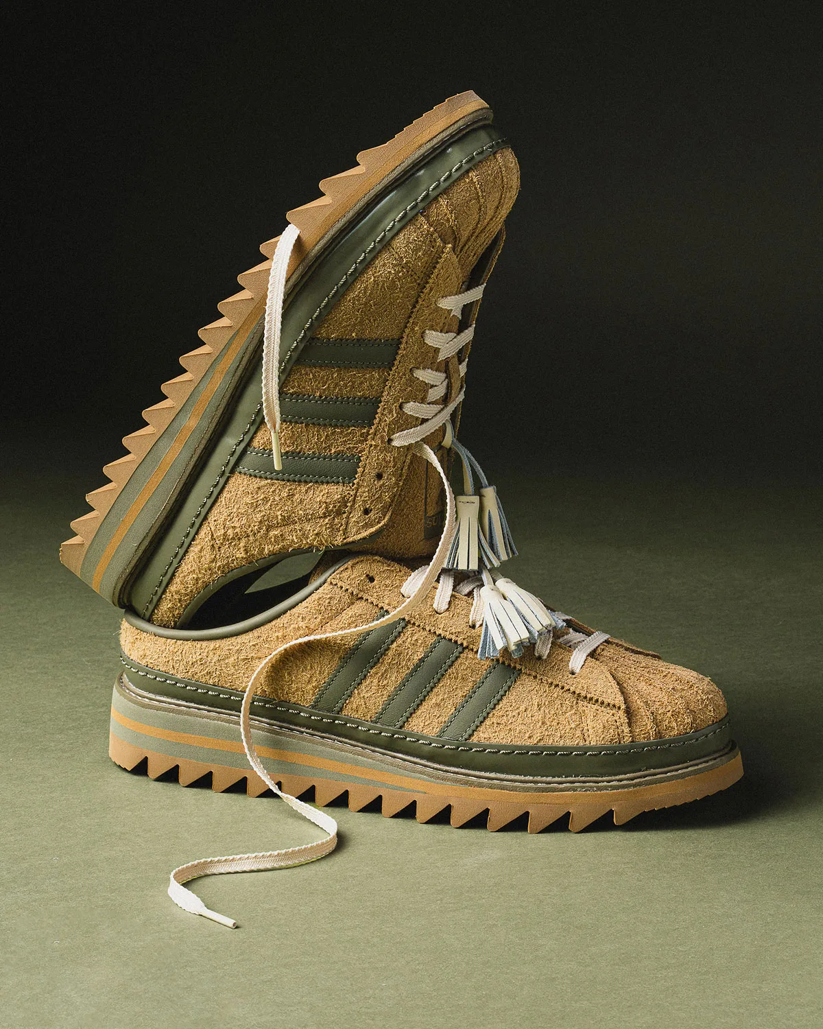 Tan suede mule propped on its pair, cream laces trailing, tassels and olive stripes visible, Mule x CLOT