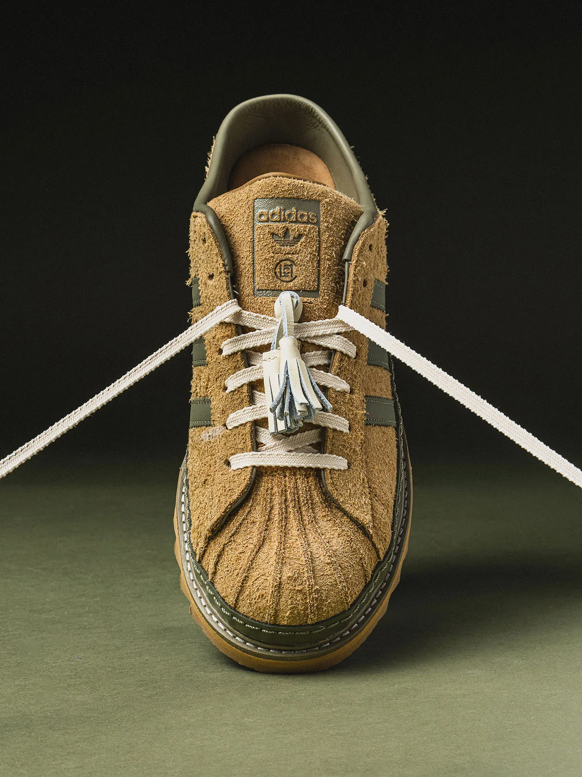 Front view of tan suede sneaker with cream tassel lace, olive stripes and adidas CLOT tongue label, Mule x CLOT