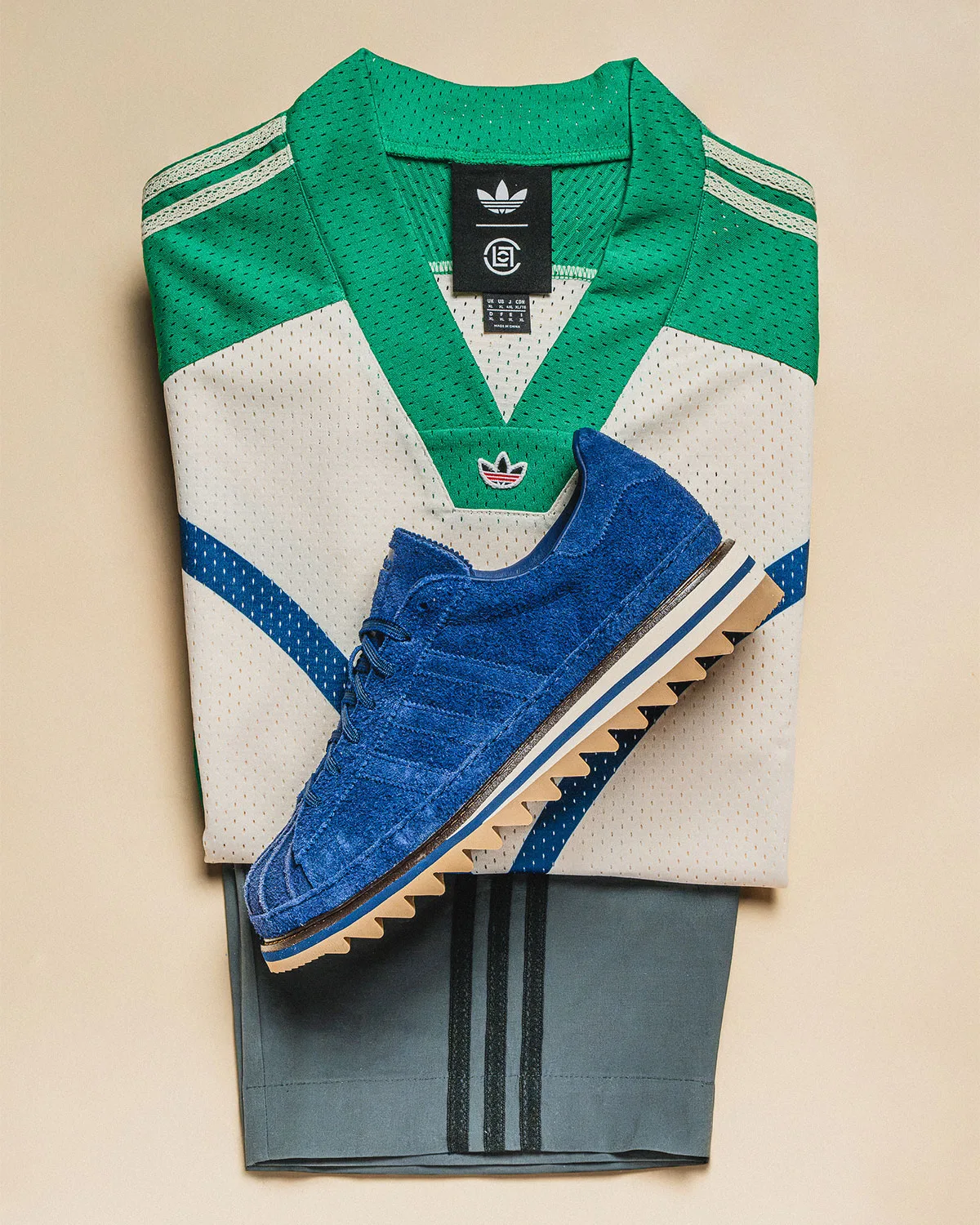 Blue suede sneaker on folded green and cream mesh jersey over grey shorts with black stripes, Mule x CLOT