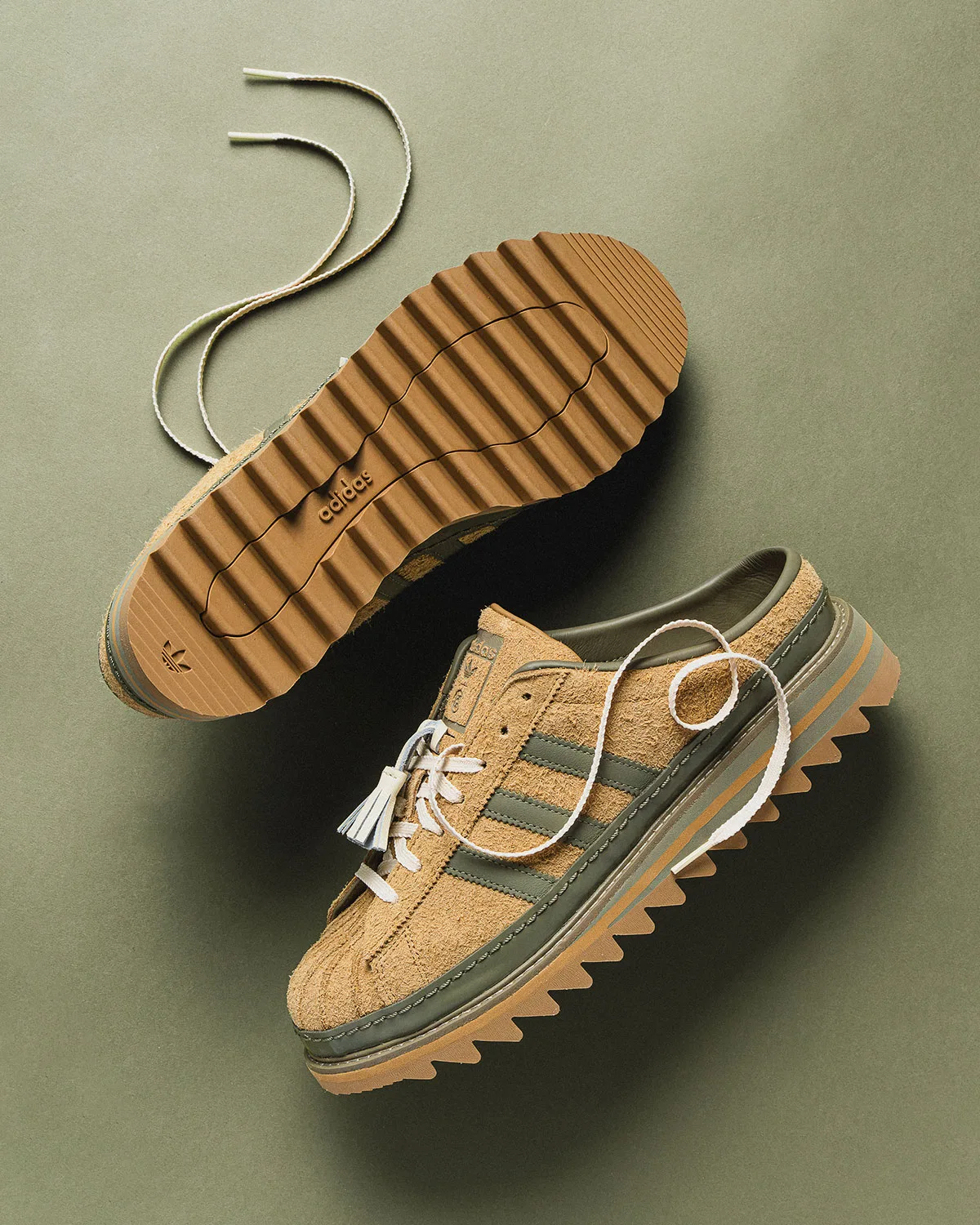 Tan suede mule outsole with ridged tread and adidas text, beside a mule with cream laces, on olive, Mule x CLOT