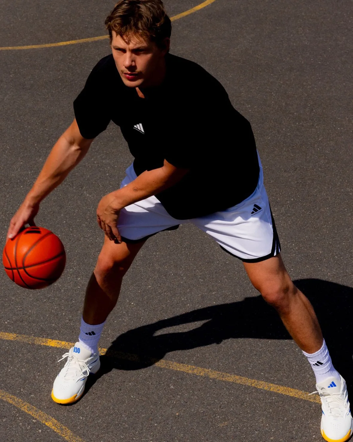 Player in a low dribbling stance on asphalt wearing white shoes with yellow soles, seen from above, Wagner Brothers