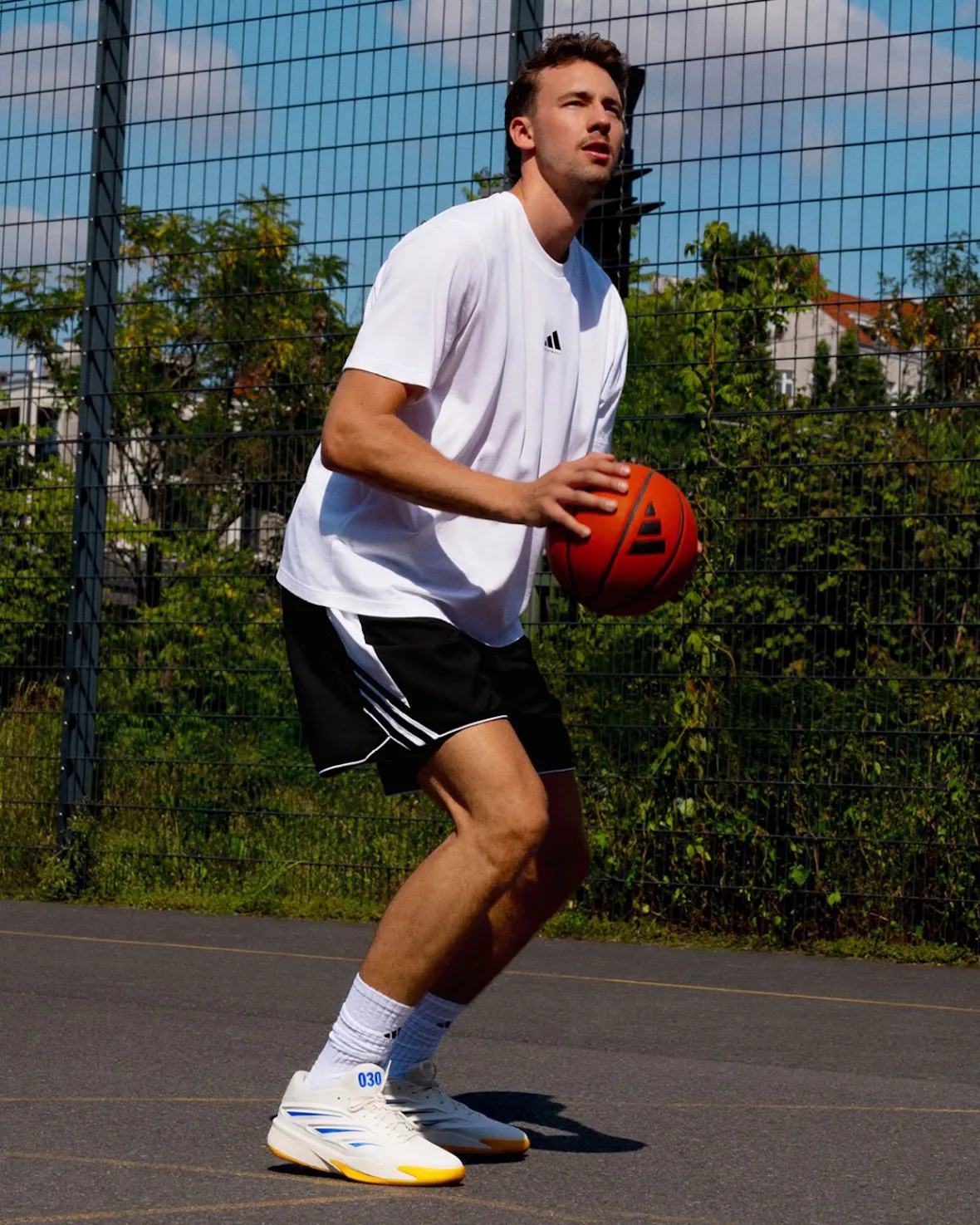 Player in white tee and black shorts holding a basketball on a fenced outdoor court, 030 shoes, Wagner Brothers