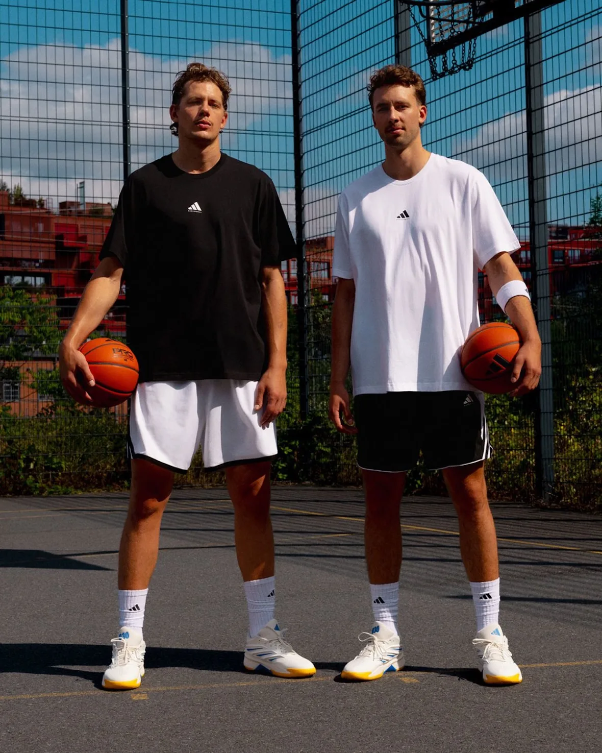 Two players in black and white outfits holding basketballs on a fenced court, wearing white sneakers, Wagner Brothers