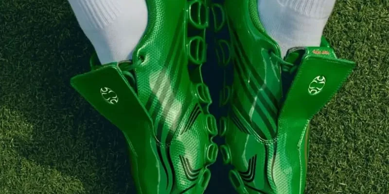 Cropped on-foot pair on turf, glossy green uppers, black stripes, oval logo on tongues, Green/Core Black/Yellow