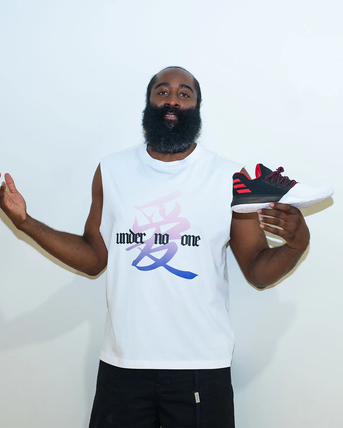 In-hand lateral view, black upper with red three stripes and white toe, held beside a white 'under no one' tank, Pioneer