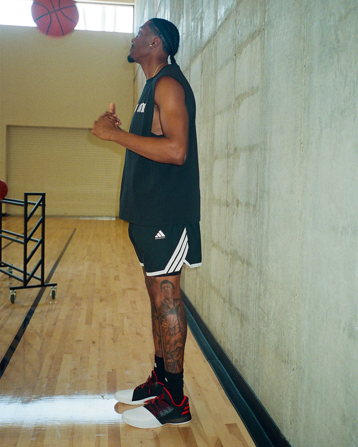 On-foot side view on a wooden court, black shoes with white toe and red accents, man in black shorts looking up at a ball