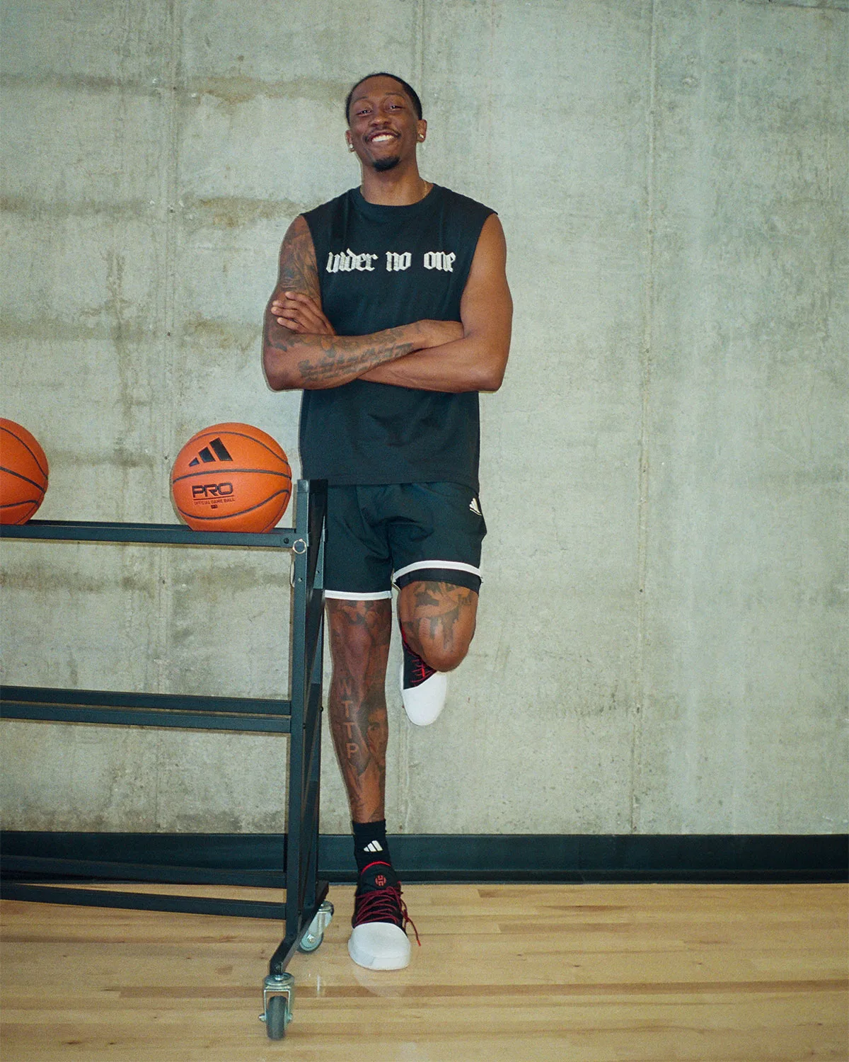 On-foot full-length shot on a gym floor, black and white shoes with red laces, concrete wall, basketballs on a rack, Pioneer