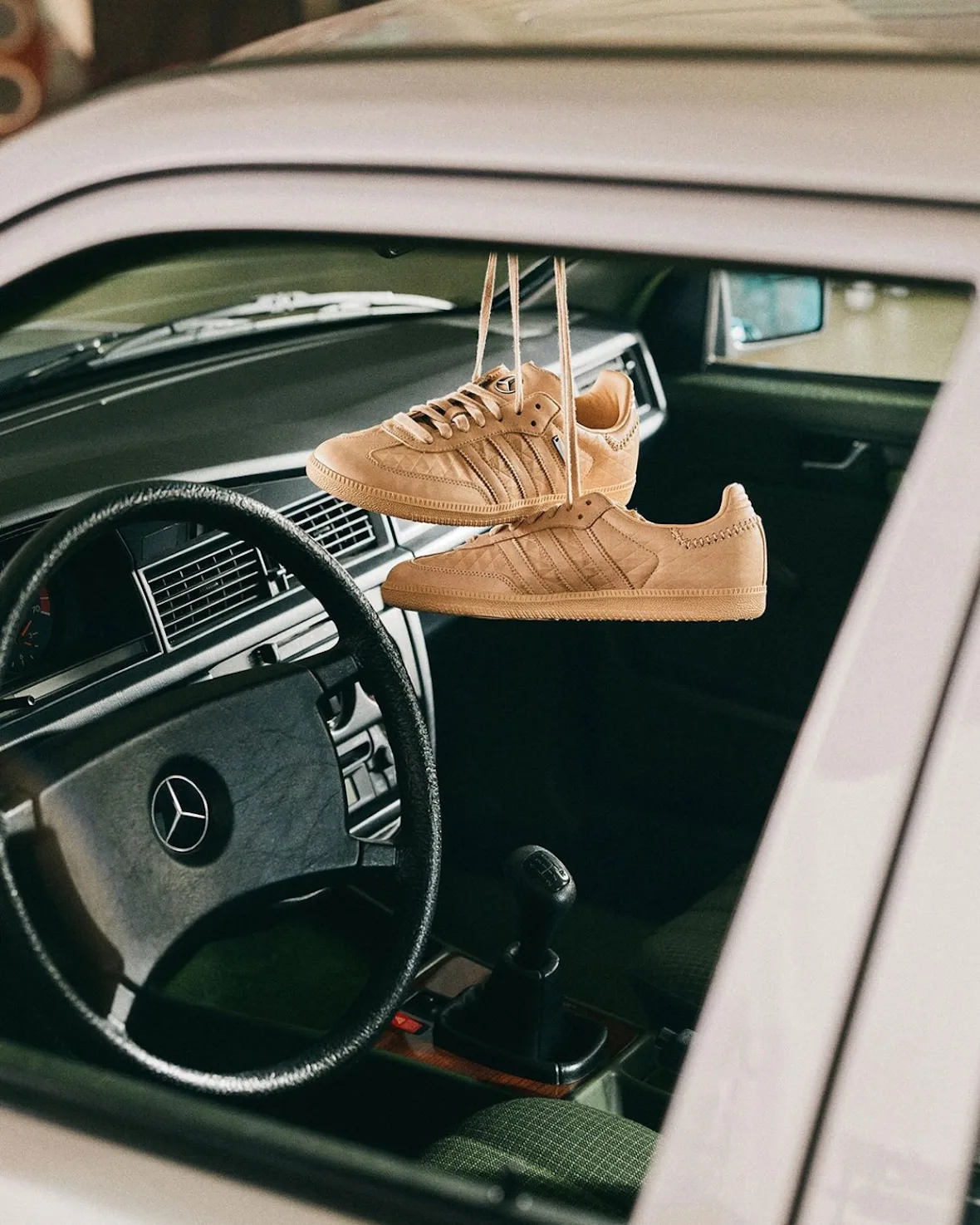 Tan sneakers hanging by laces inside a car, steering wheel with star logo behind, x Mercedes Benz