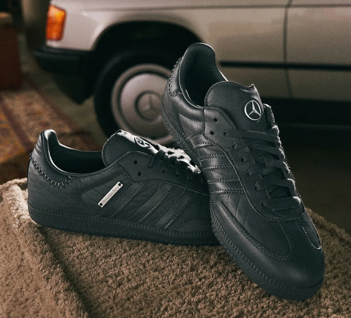 Pair of black leather sneakers with silver star badges on a beige fleece, car wheel behind, x Mercedes Benz