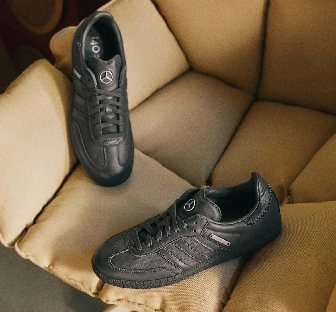 Top-down pair of dark grey leather sneakers with star badges on a mustard puffy armchair, x Mercedes Benz