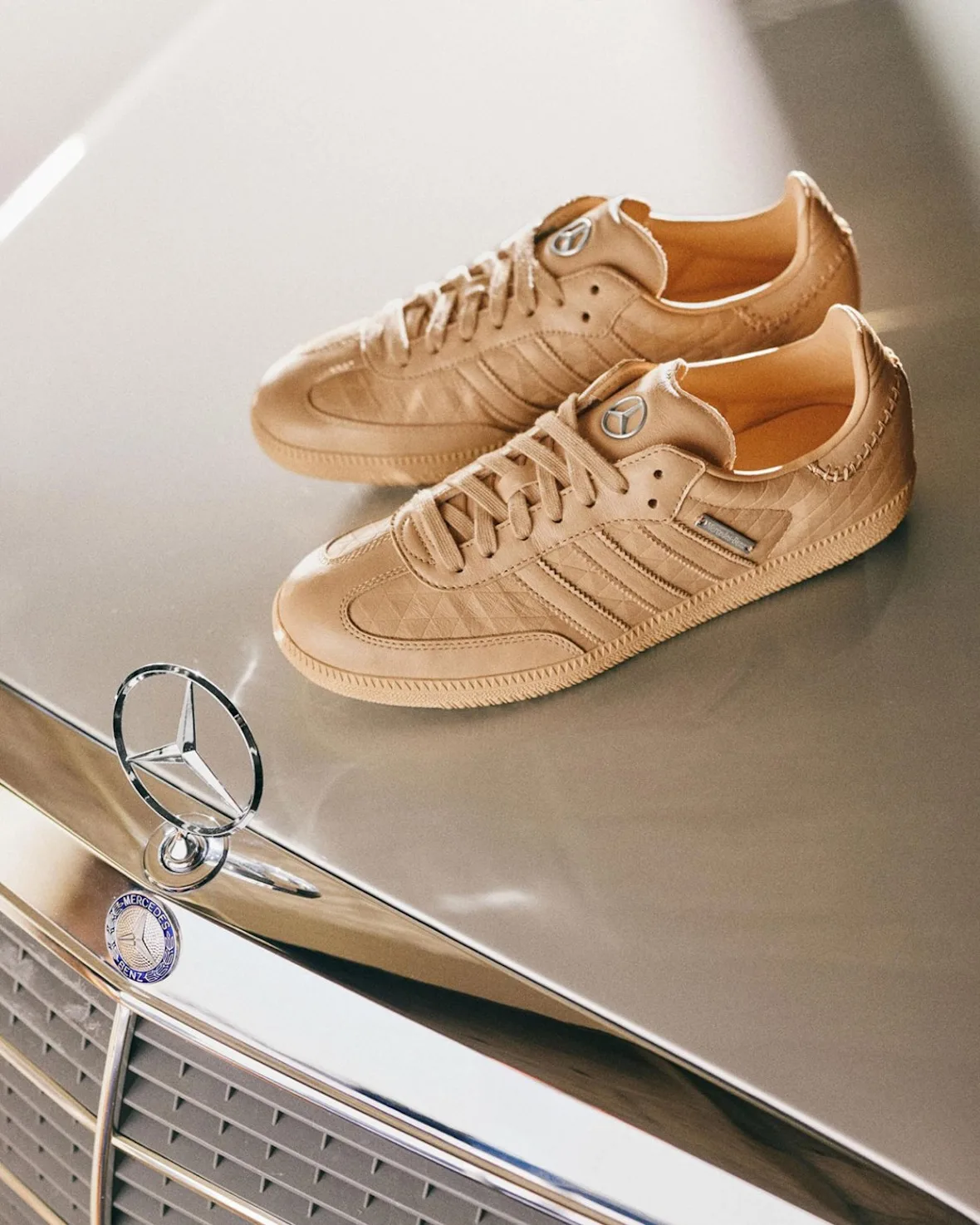 Pair of tan quilted-leather sneakers with gum soles on a car bonnet beside a star hood ornament, x Mercedes Benz