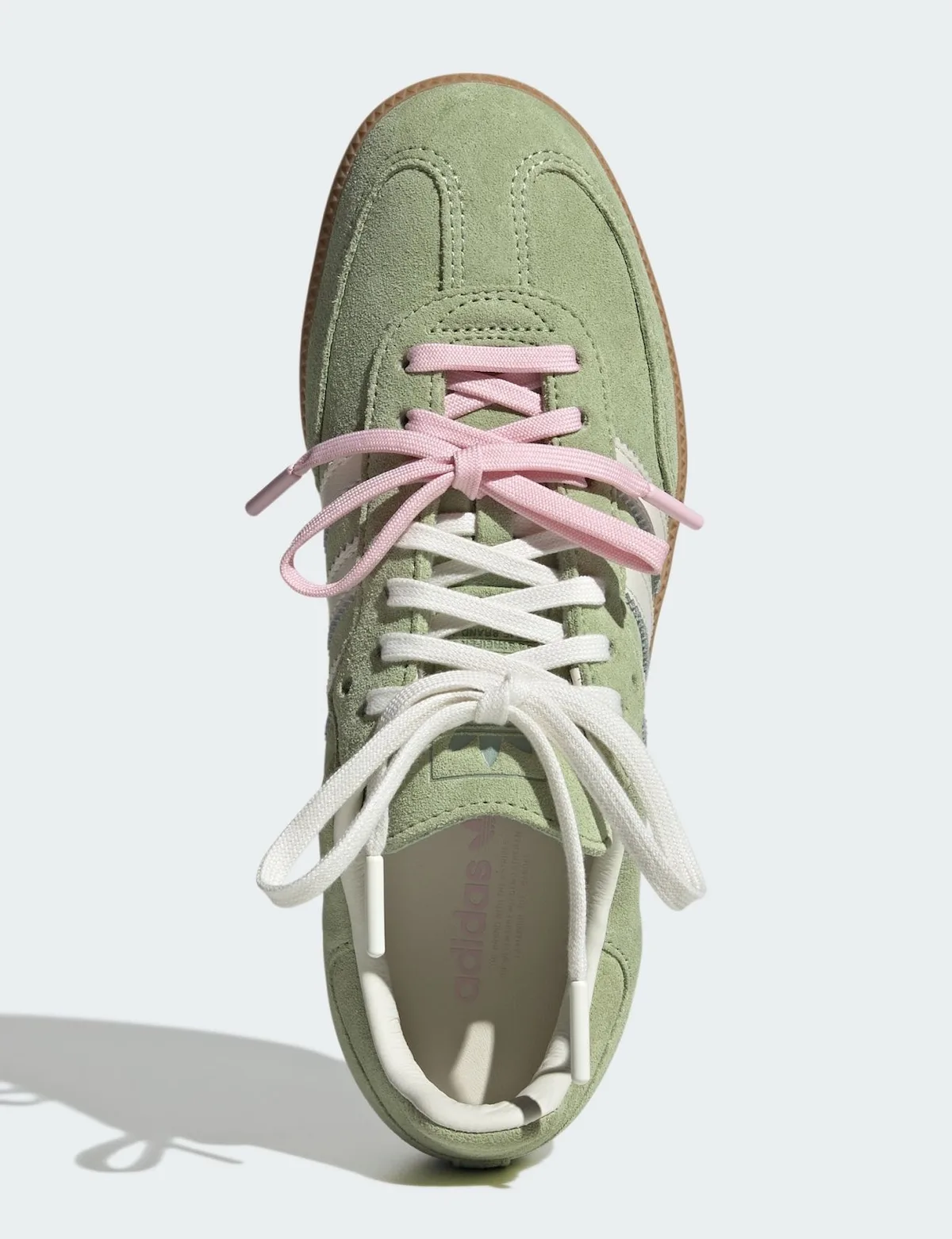 Top-down view of green suede sneaker with pink and cream laces tied in bows, Matcha