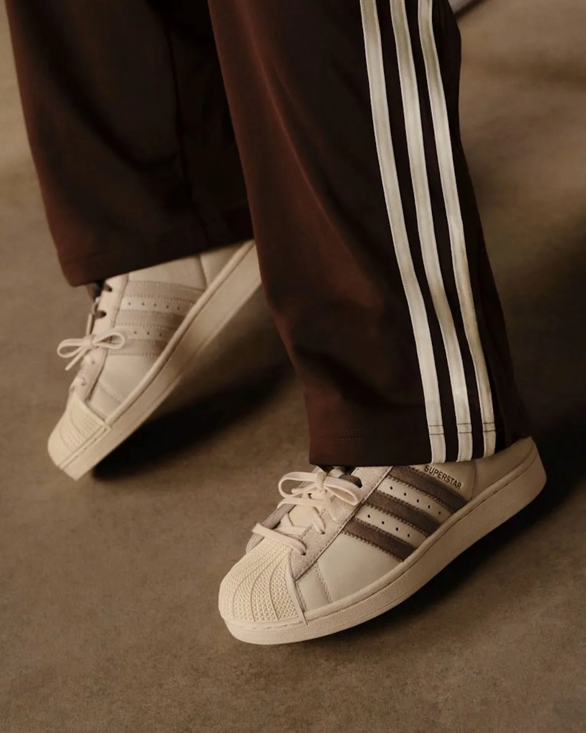 On-foot shot of cream Superstar with brown stripes, brown track pants with cream stripes, Matcha