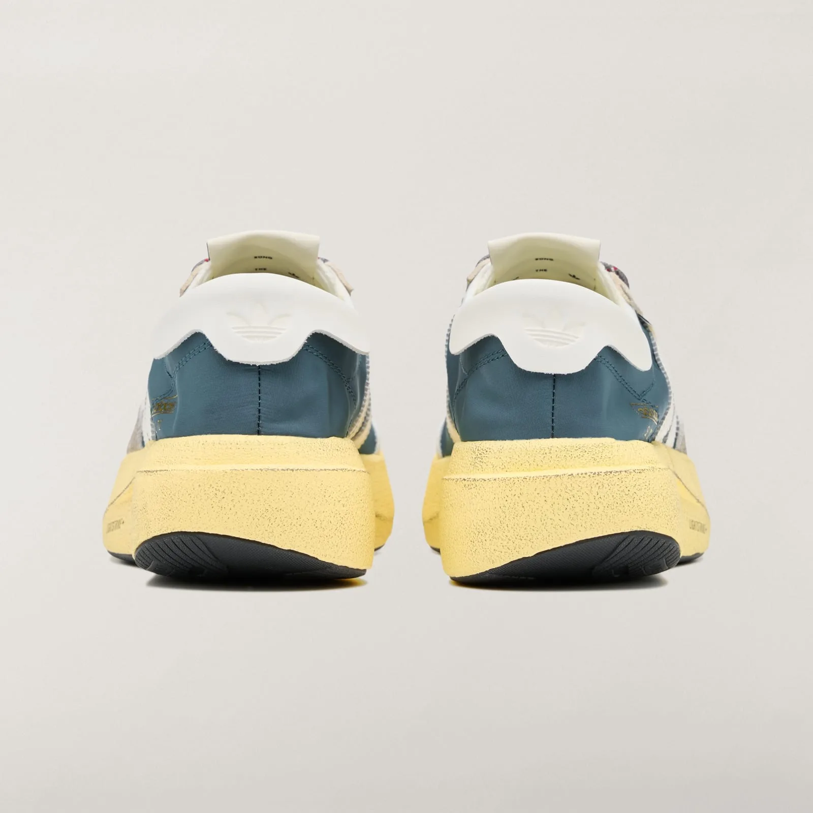 Heel view of pair with white Trefoil tabs and thick yellow soles, Wild Teal