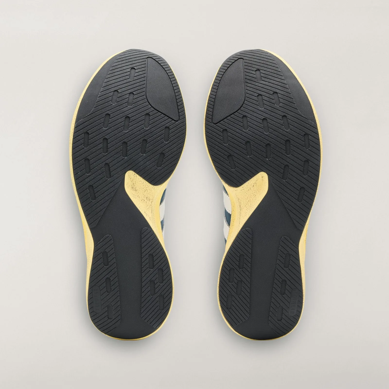 Outsole view of pair with black grooved tread and yellow midfoot cutouts, Wild Teal