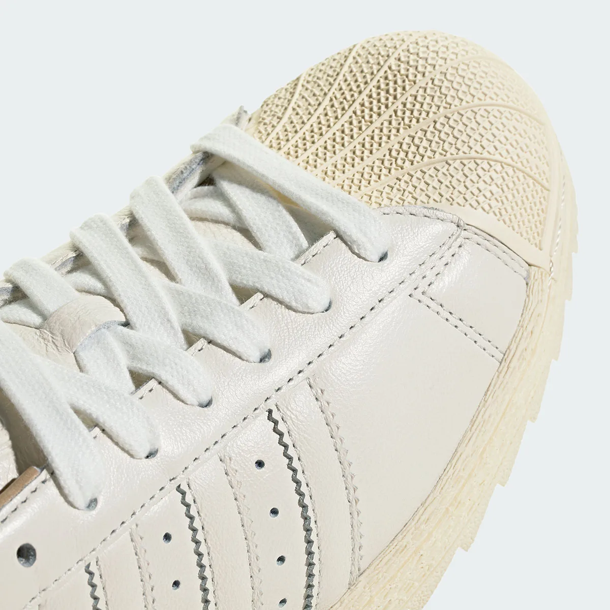 Close-up of cream shell toe texture, white flat laces and stitched off-white leather stripes, Core White