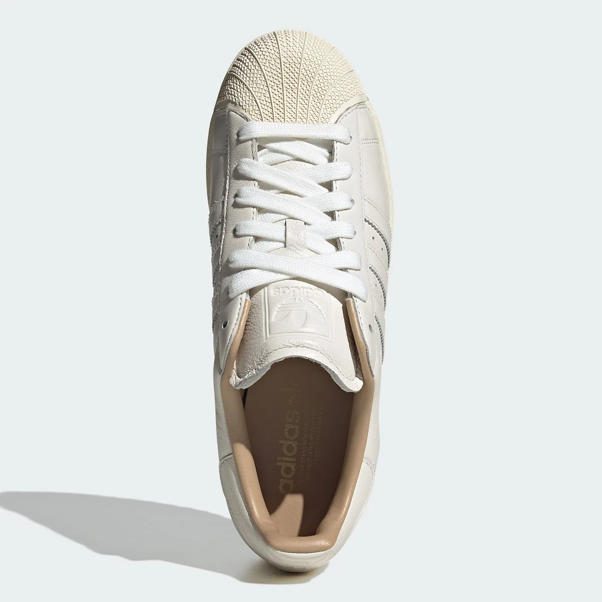 Top-down view of white laces, embossed tongue logo and tan insole with adidas text, Core White