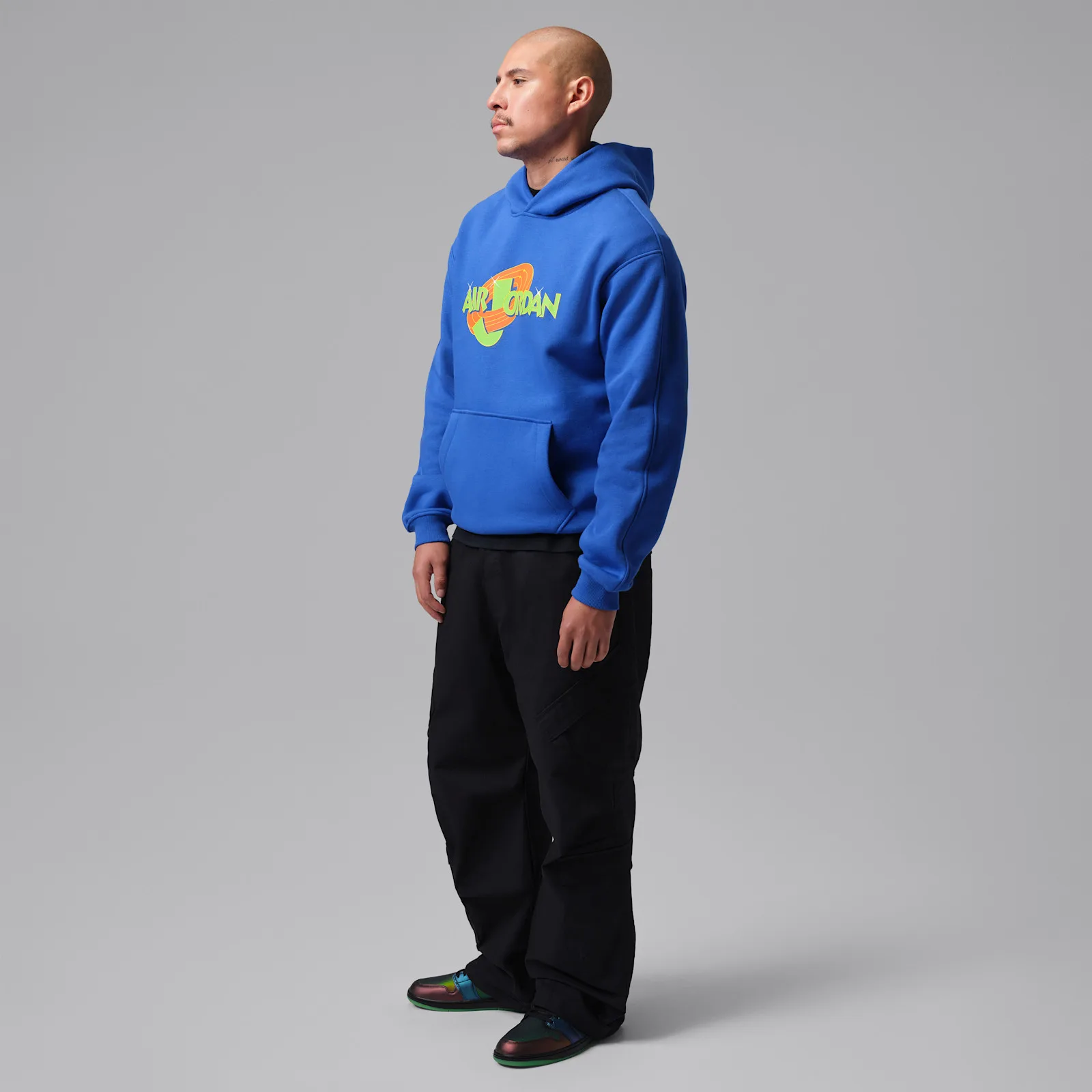 On-foot view of person in blue hoodie with green Air Jordan graphic and black trousers, Air Bugs