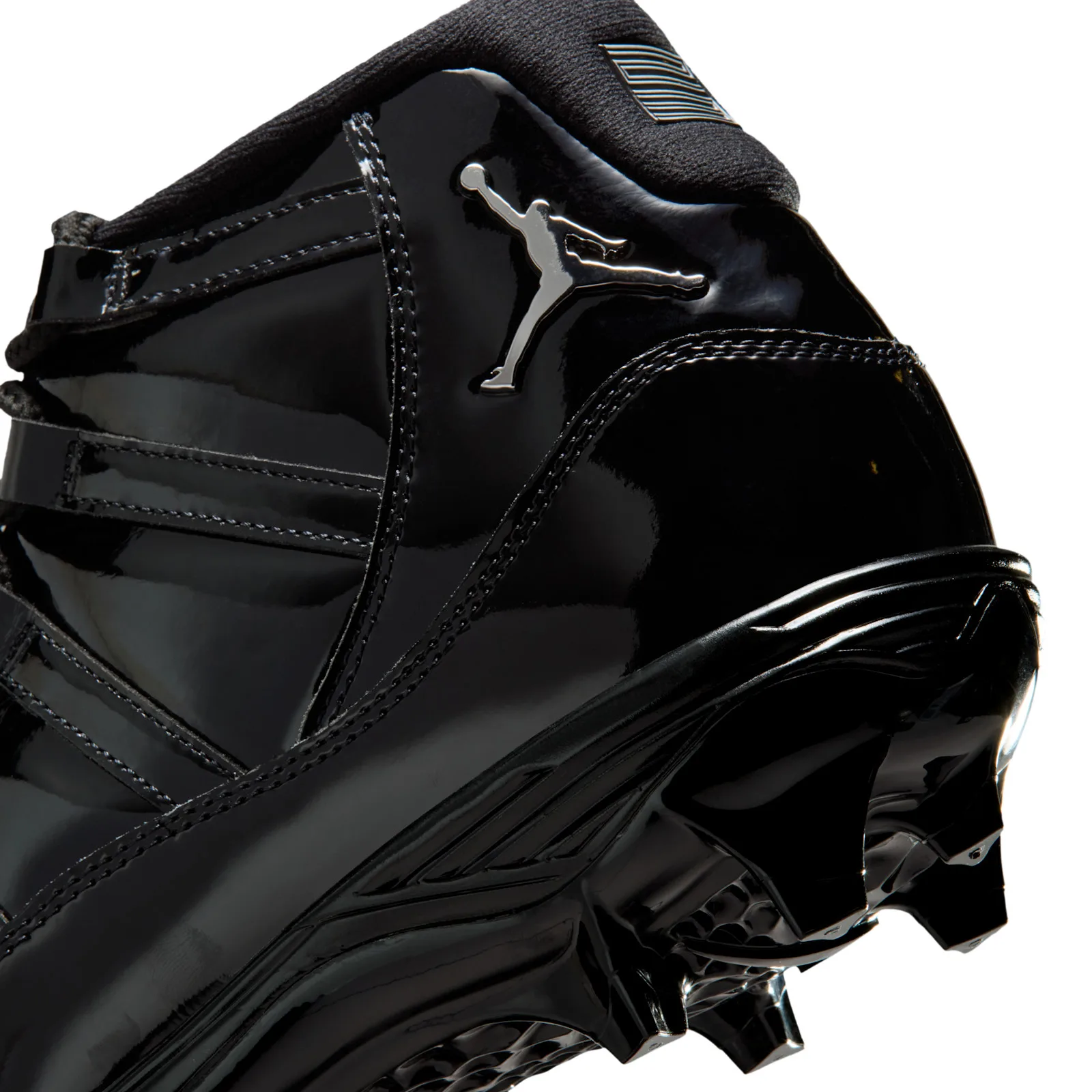 Detail of silver Jumpman logo on glossy black patent heel, with stitching and cleat studs below, Gammas