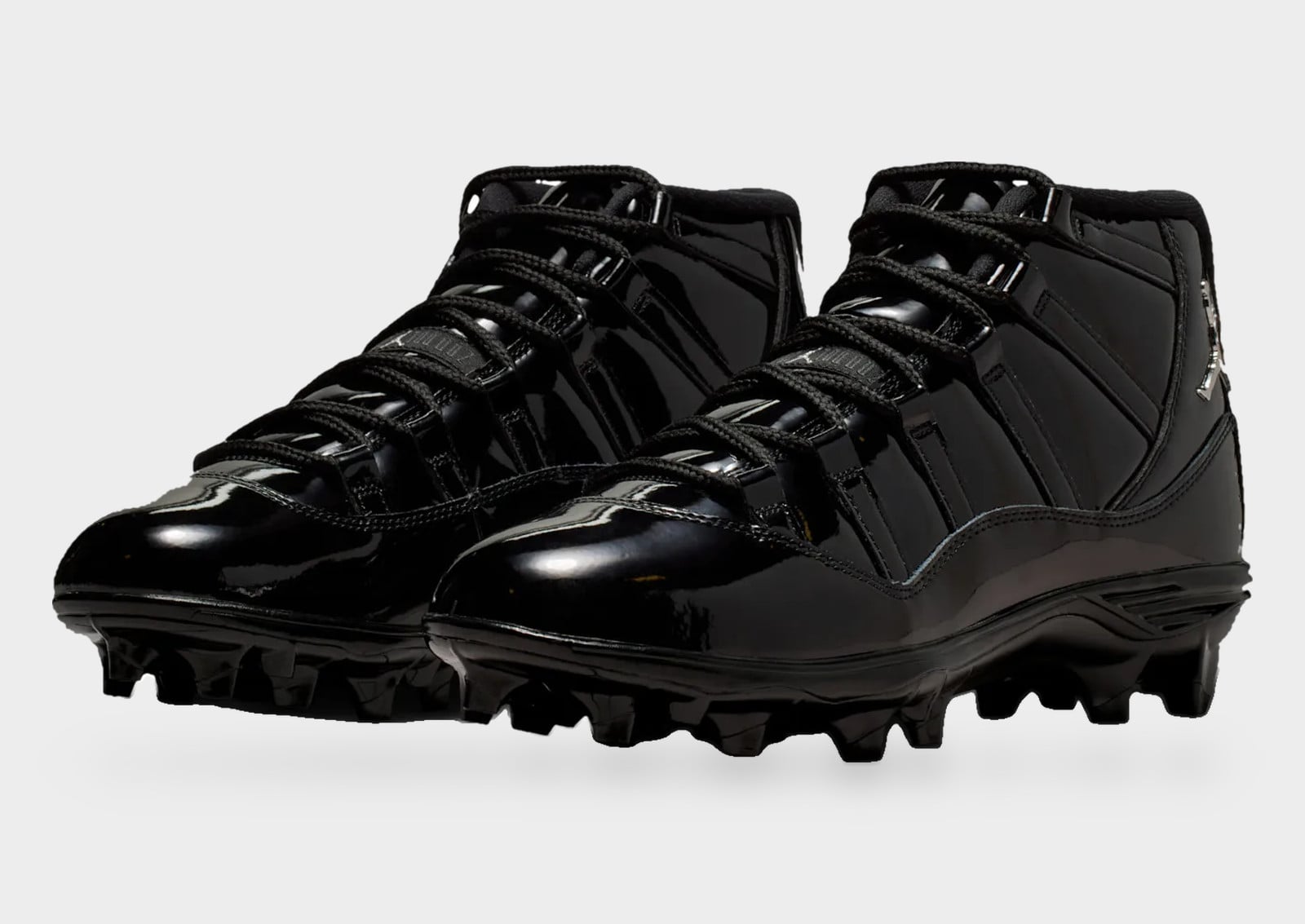 Pair at three-quarter angle, all-black glossy patent cleats with black laces, Air Jordan 11 “Gammas” UCLA Football Cleat PE