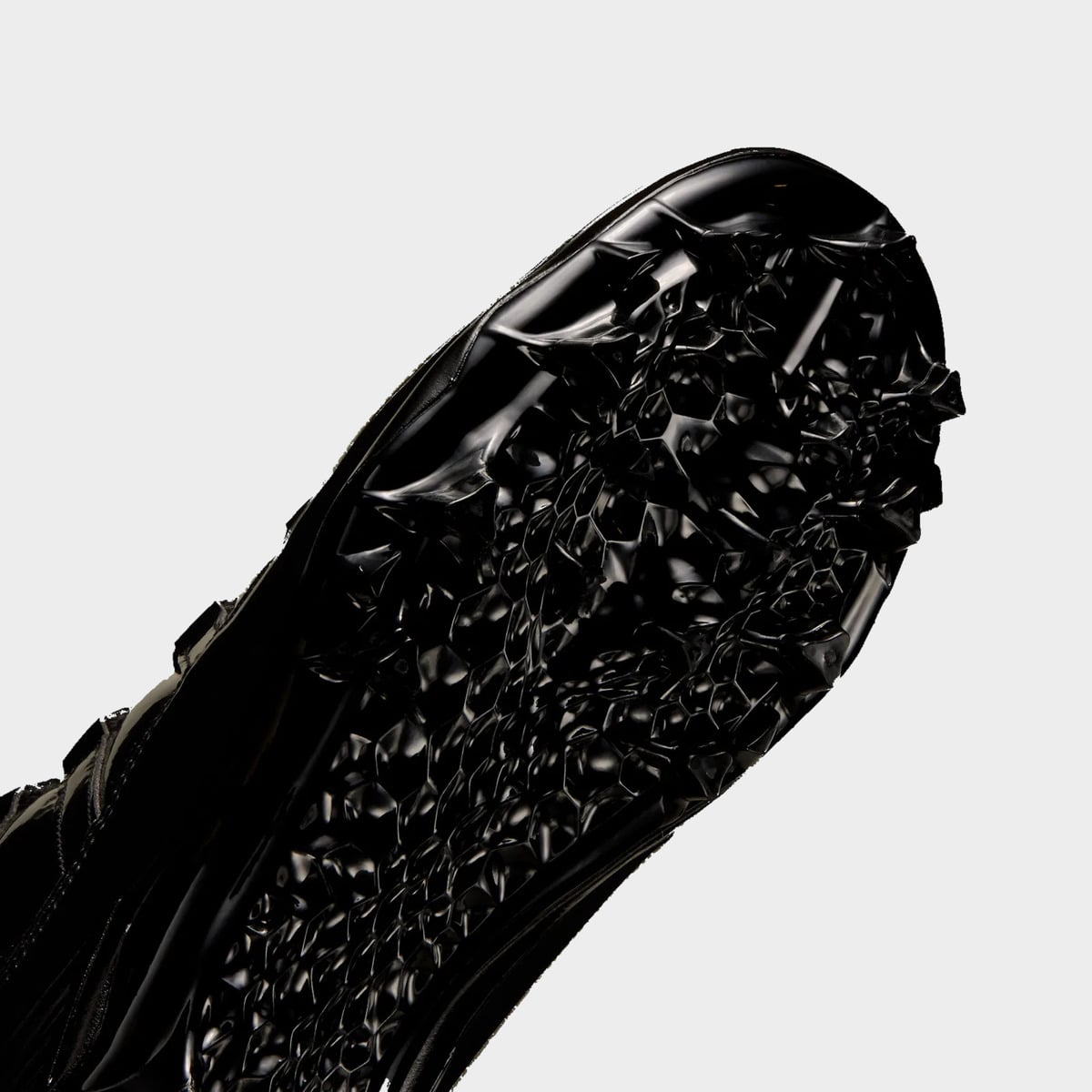 Detail of black cleat forefoot outsole, angled to show textured traction pattern and studs, Gammas