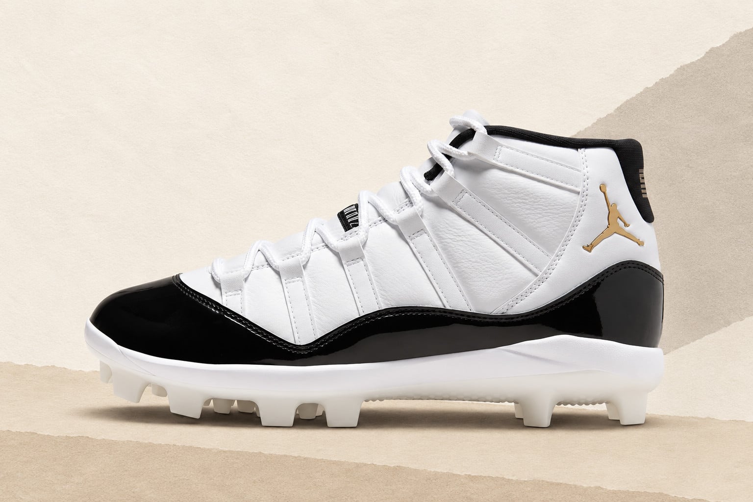 Lateral view of white leather cleat with black patent toe, gold Jumpman logo, on beige paper, Air Jordan 11 MCS Cleats “DMP”