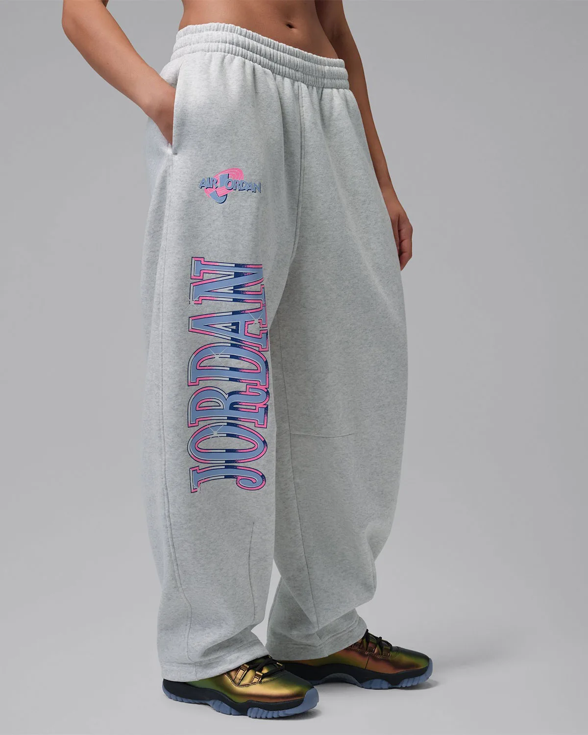 on-foot detail, grey sweatpants with pink and blue Air Jordan logo and Jordan wordmark, gold sneaker visible, WMNS Space Jam
