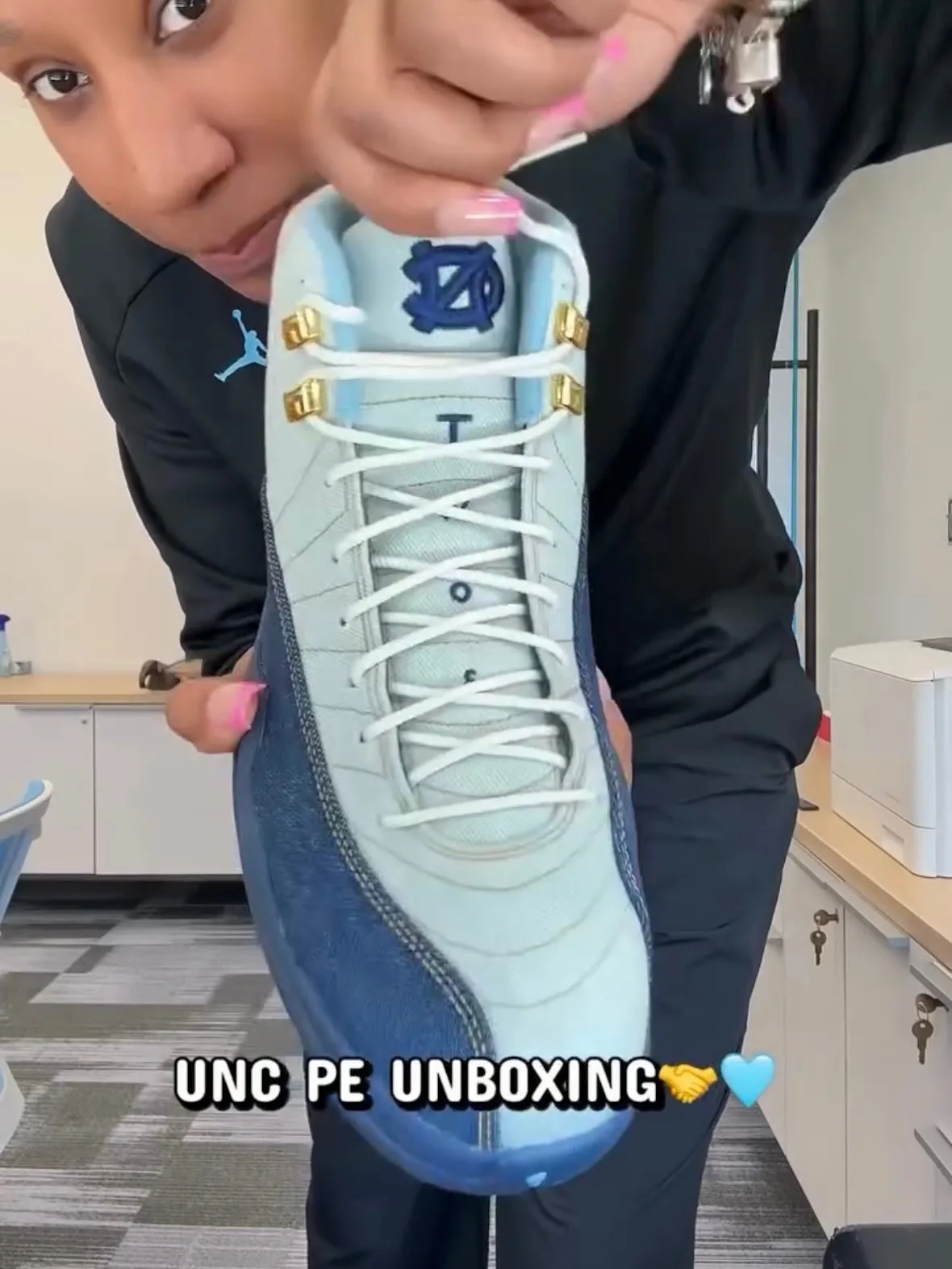 In-hand top-down view of laced shoe with NC logo, held by person in black Jordan top, UNC