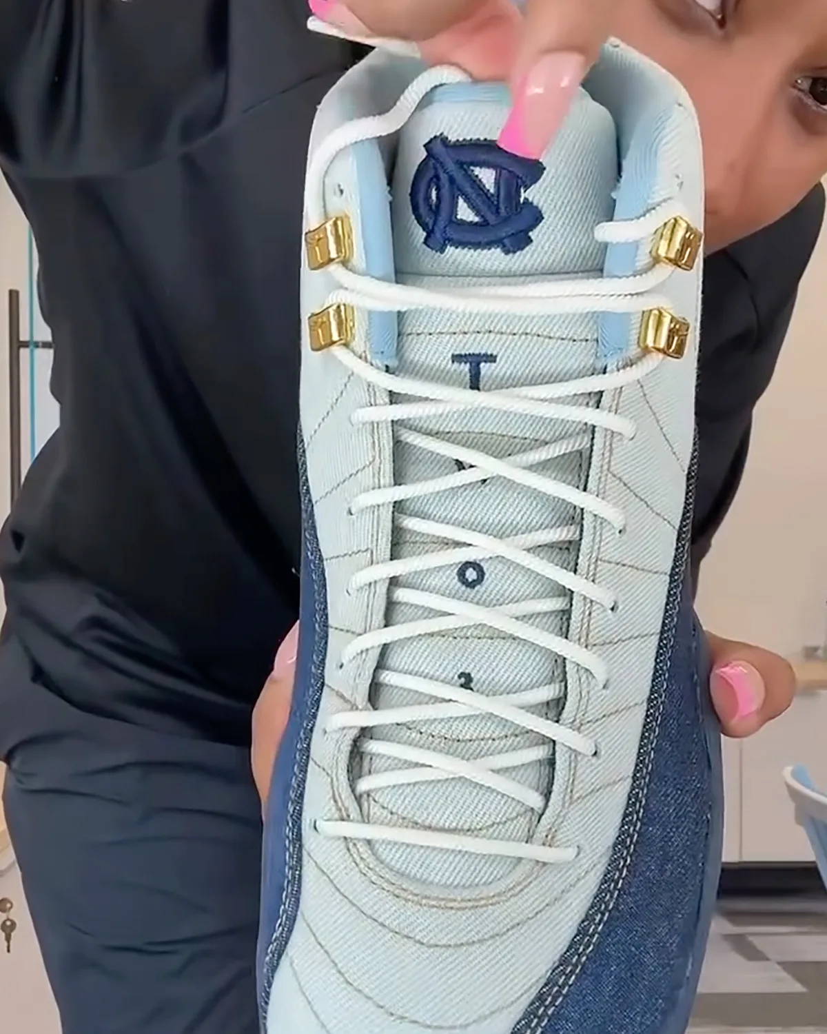 Top-down in-hand view of white laces, gold eyelets and navy NC logo on tongue, UNC