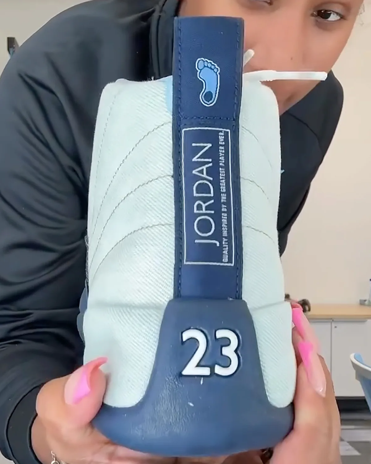 In-hand heel view of navy tab with blue footprint logo, Jordan text and white 23, UNC