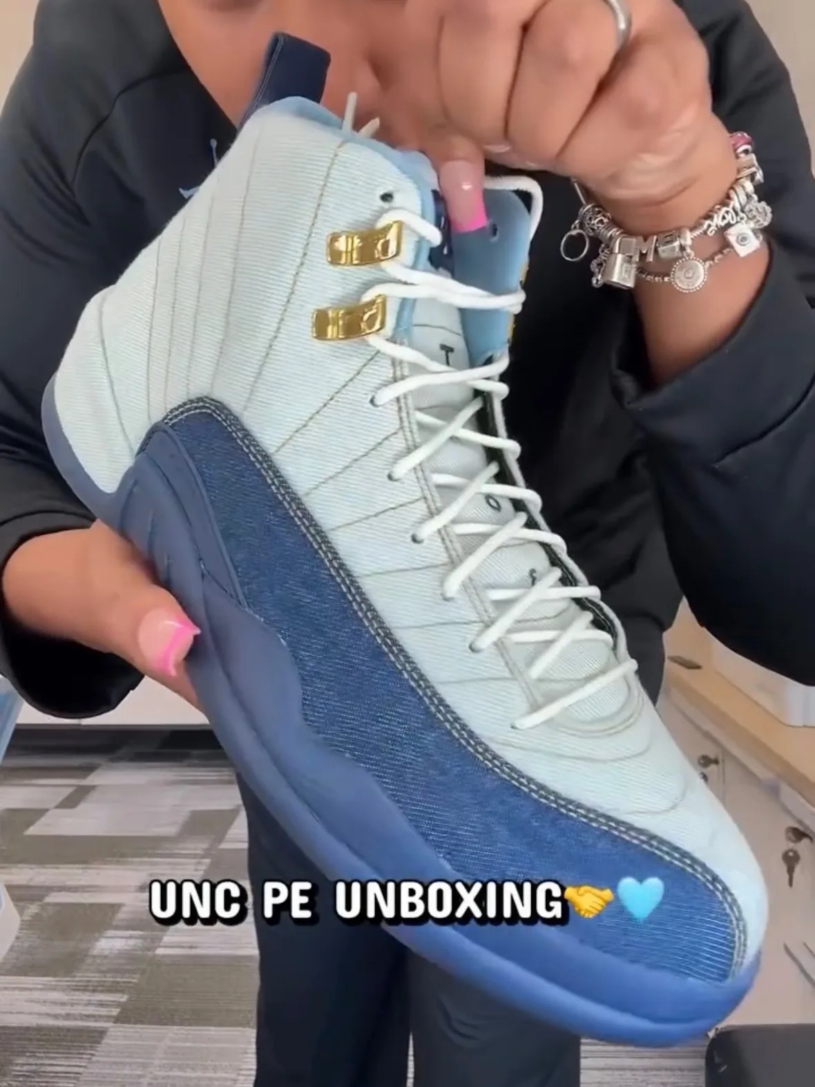 In-hand lateral view of pale blue and denim shoe, gold eyelets, UNC PE unboxing caption, UNC