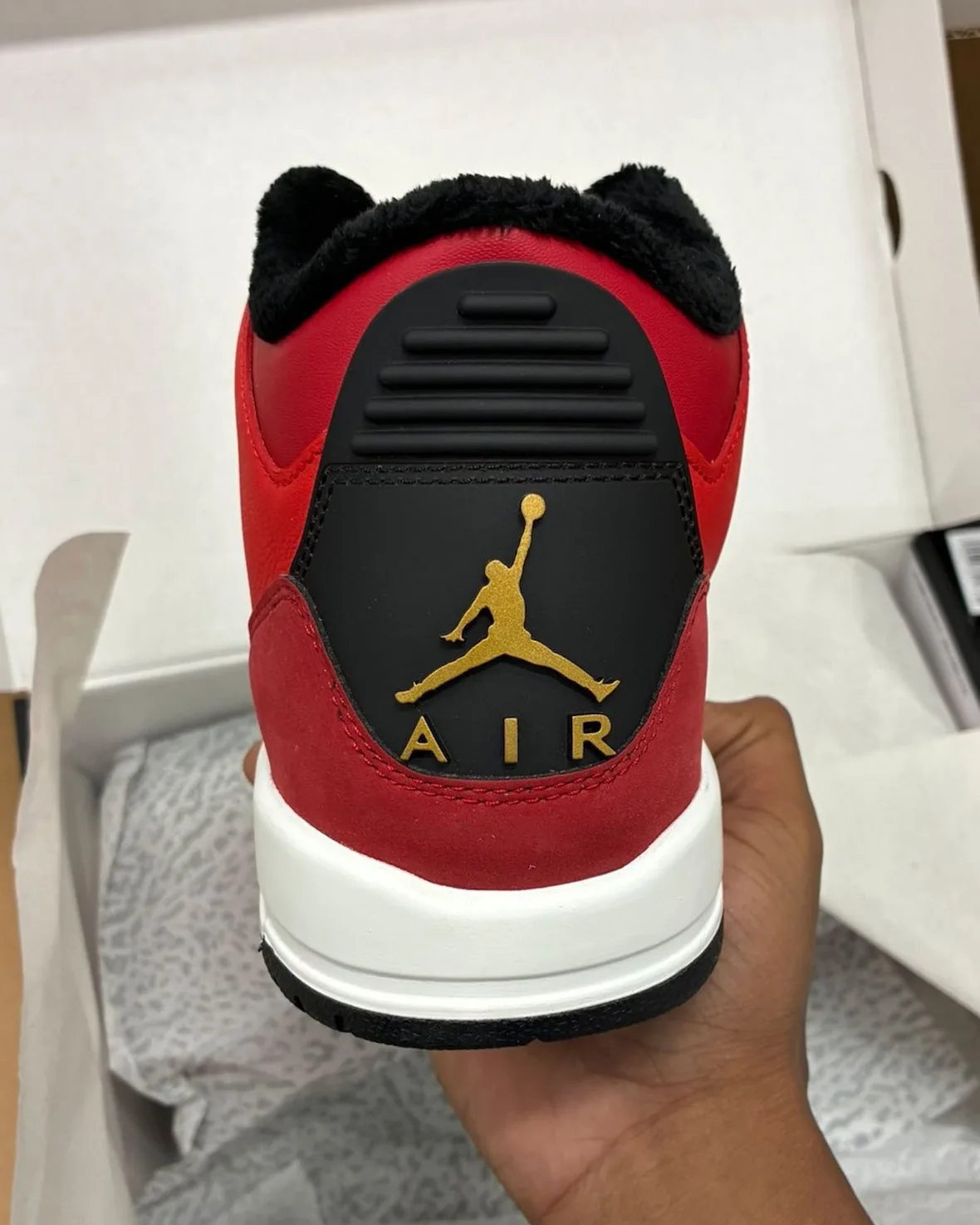 Heel view in hand, gold Jumpman and AIR on black heel tab, red suede, black fleece collar, Santa