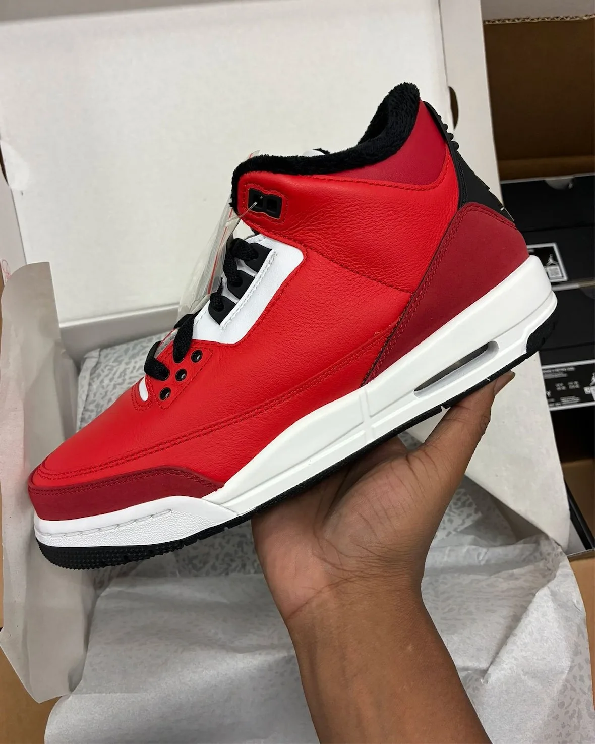 Lateral view held in hand in a box, red leather upper, white midsole, black fleece collar, Santa