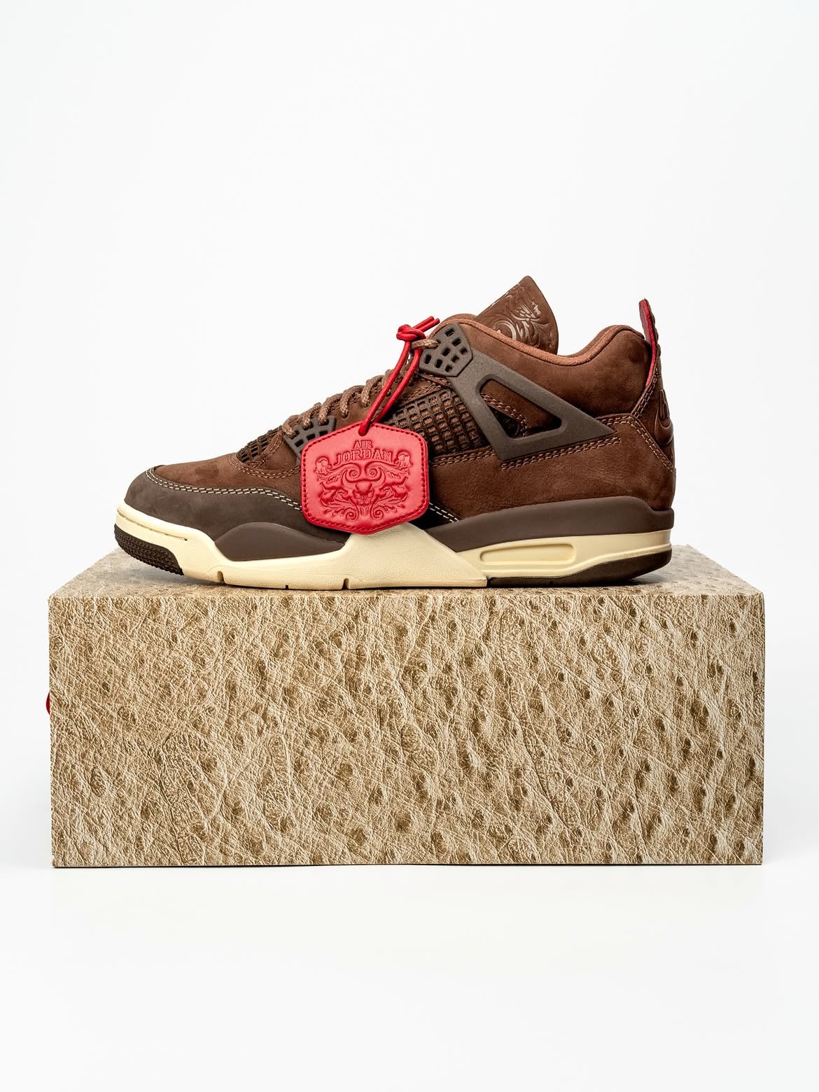 Lateral view on textured ostrich-print box, brown suede, cream midsole, red hangtag, Bin23