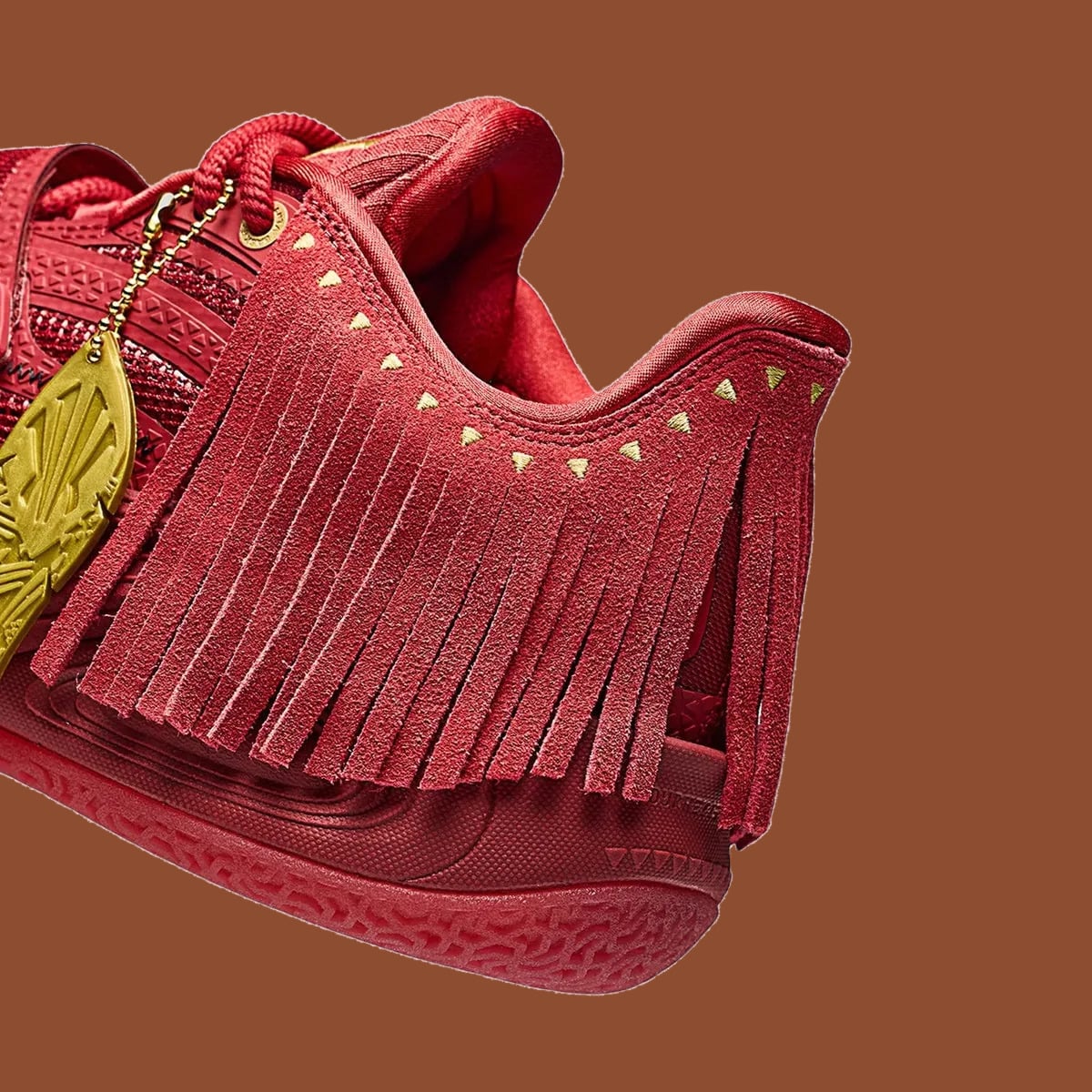 Detail of heel, red suede fringe with gold triangle studs beside gold charm, Red