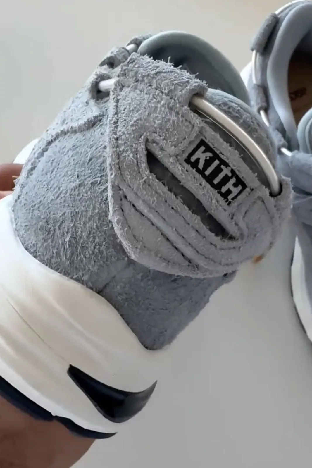Heel detail held in hand, blue-grey suede tab with black KITH box logo, x Giorgio Armani
