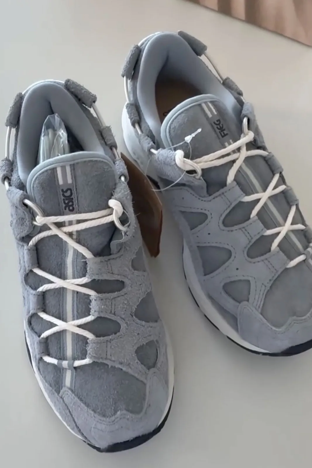 Top-down pair on a pale surface, blue-grey suede, white rope laces, hang tag, x Giorgio Armani