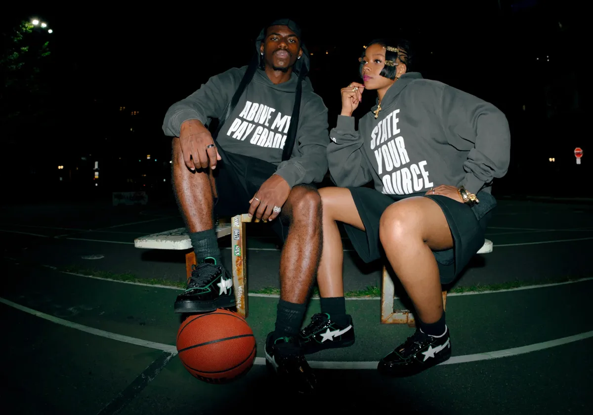Two people seated on a bench at night in grey hoodies, wearing black sneakers, basketball by their feet, STA x 7UICE