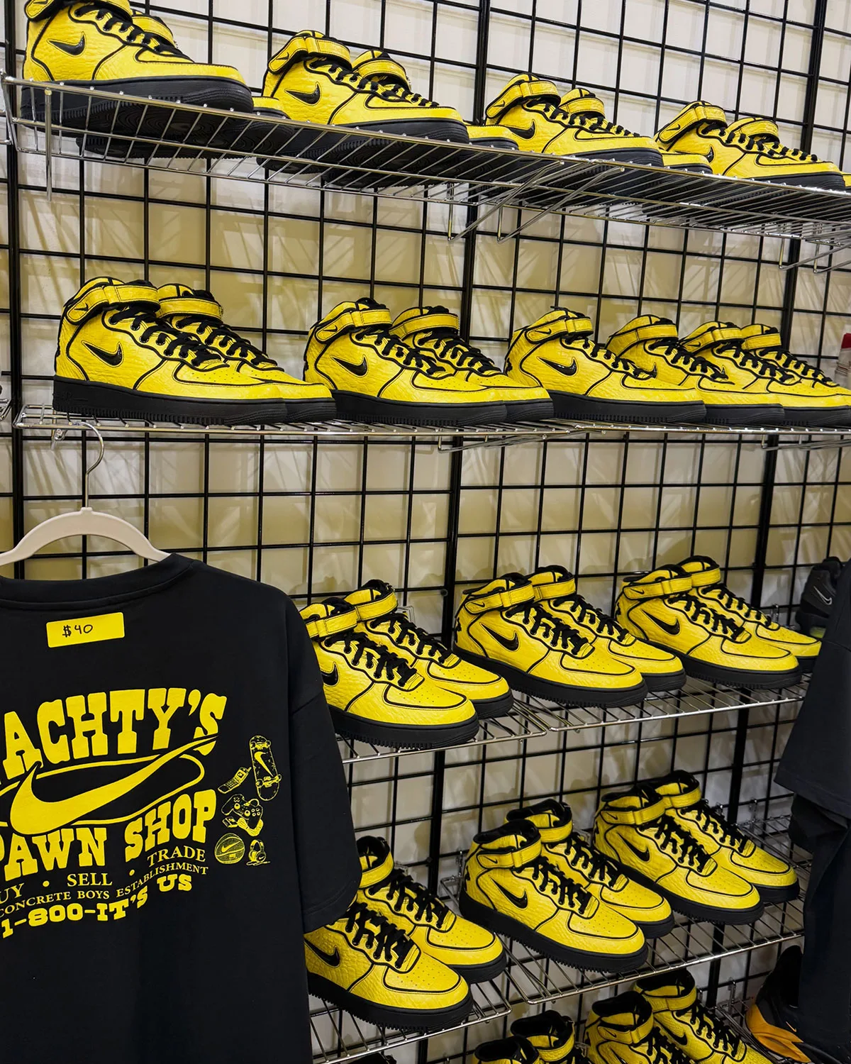 Wall display of yellow mids on wire shelves beside a black "Pawn Shop" tee marked $40, Force 1 Mid