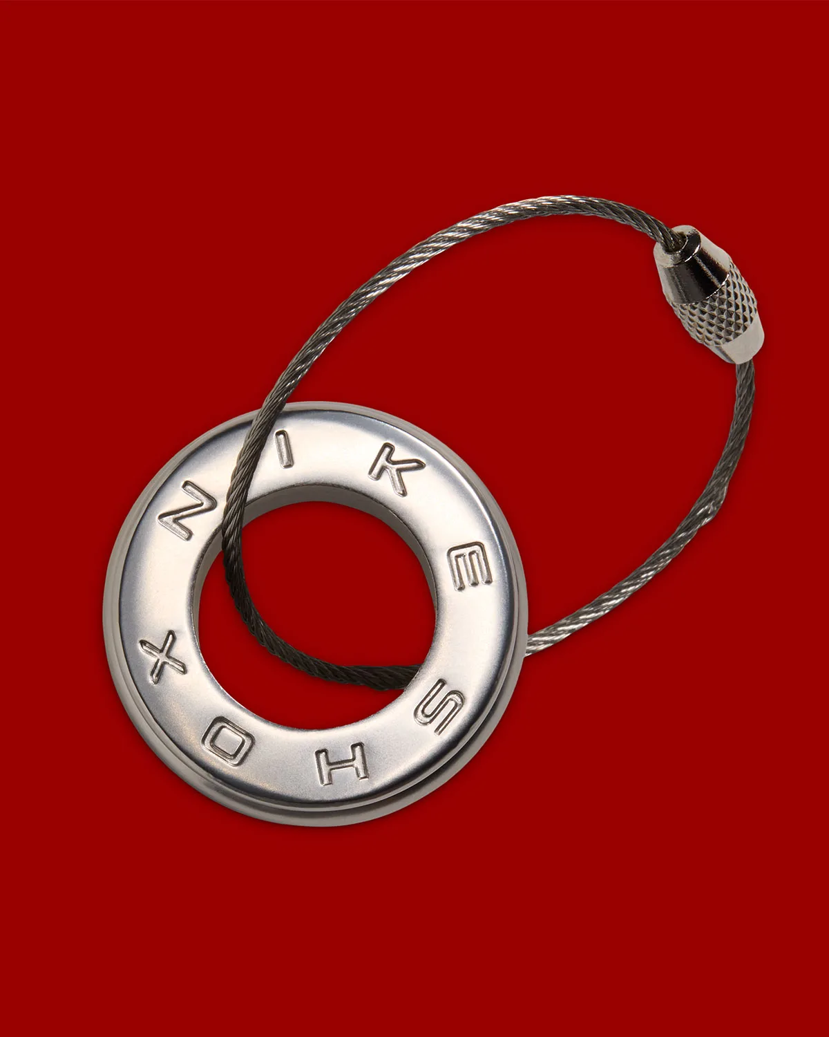Detail: silver ring keychain stamped NIKE SHOX with a braided steel cable loop, red backdrop, Game Royal