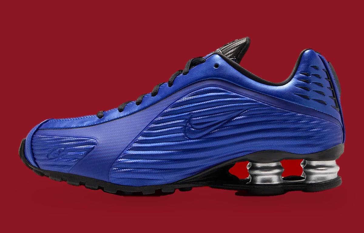 Lateral view: blue ridged upper with tonal swoosh, black laces, silver heel springs, red backdrop, Game Royal