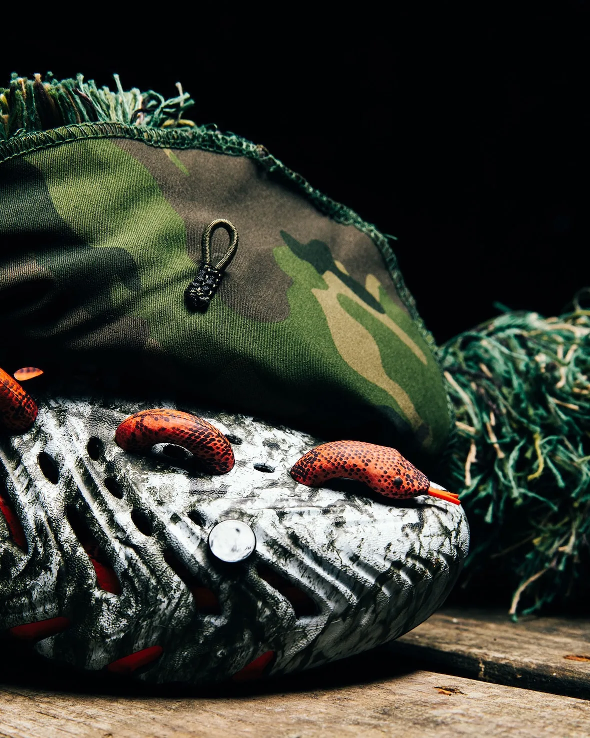 Toe detail with orange snake charms on marbled clog, camouflage fabric and green fringe behind, on wood, Watch Your Step
