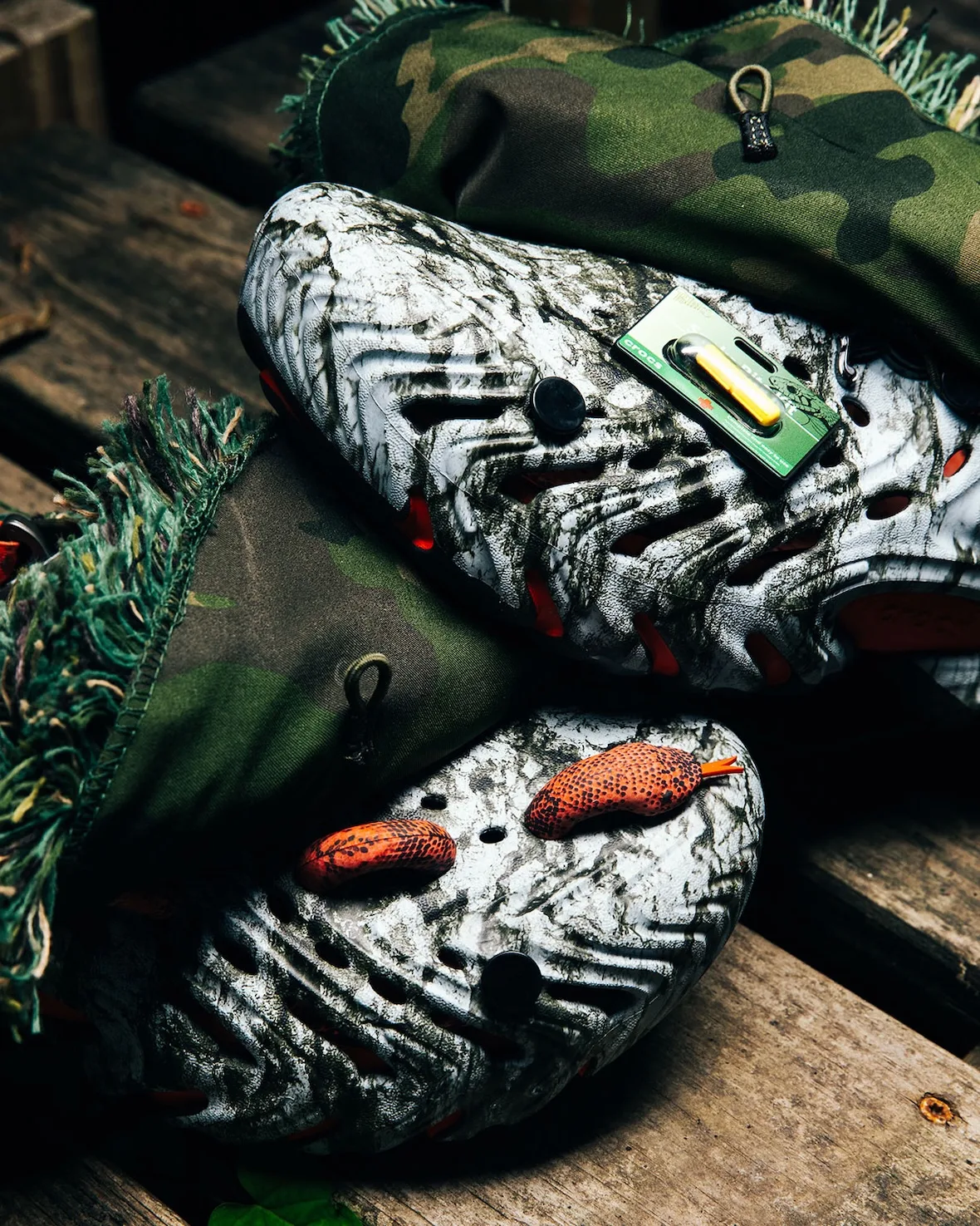 Camouflage fabric covers on marbled clogs, orange snake charms, green Snake Bite Kit charm, on wood planks, Watch Your Step