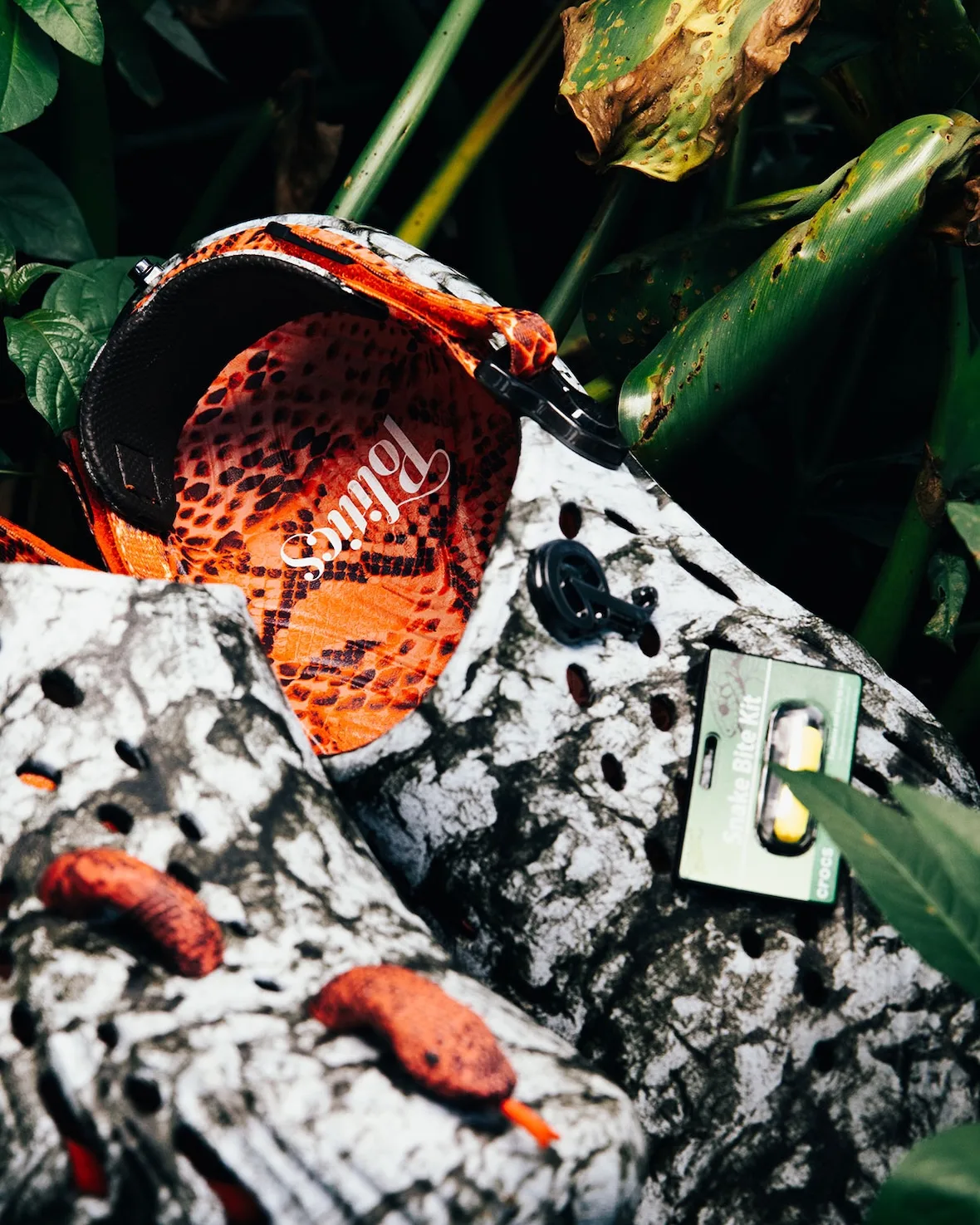Detail of orange snakeskin footbed with white Politics script, Snake Bite Kit charm, marbled clogs, green foliage, Watch