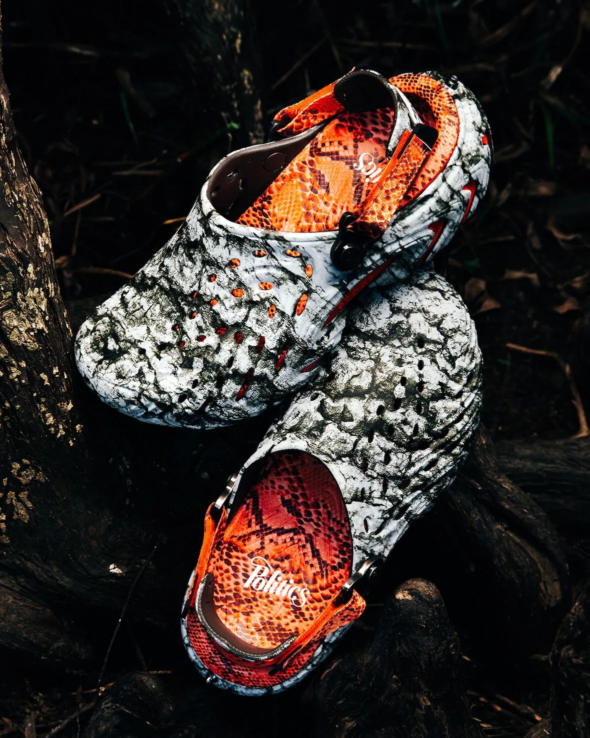 Top-down pair on roots, marbled white and black clogs, orange snakeskin footbed with white Politics script, Watch Your Step