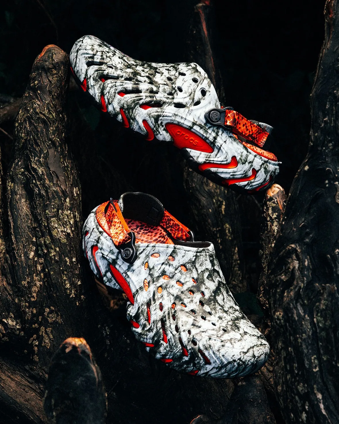 Pair on dark tree roots, marbled grey-white clogs with orange outsole pods and orange snakeskin heel straps, Watch Your Step
