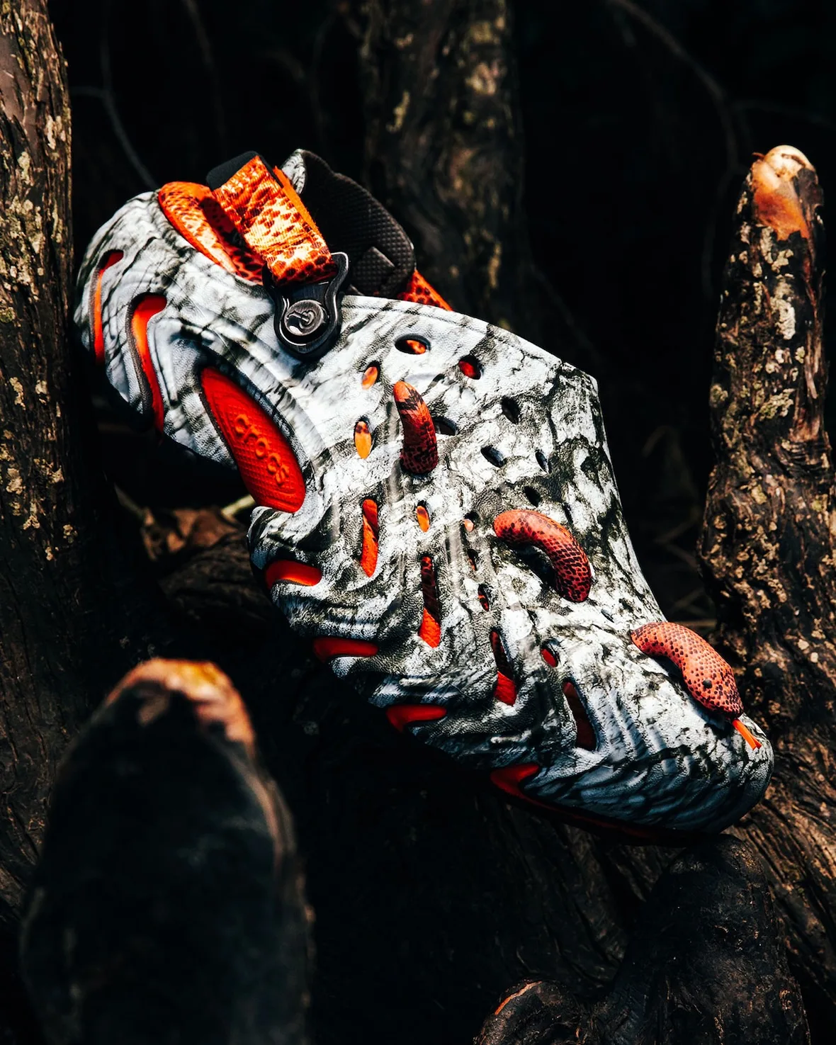 Lateral angled view, grey-white marbled clog with orange snake charms and orange snakeskin heel strap on dark roots, Watch