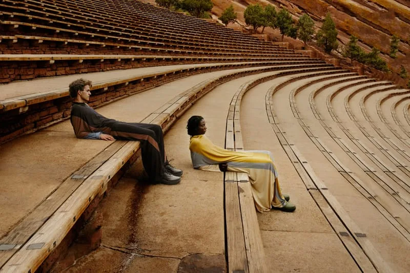 Two seated models in an outdoor amphitheatre with brick-red steps, one in black shoes, one in green, x Kiko Kostadinov