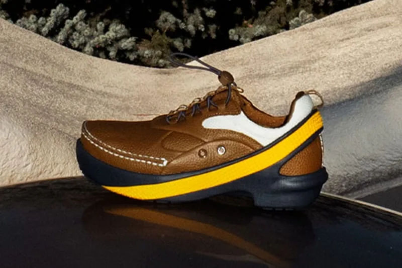 Lateral view of brown leather shoe with yellow midsole stripe, cream heel panel and navy sole against sand-coloured rock, x