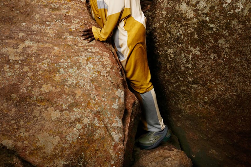 On-foot view of grey-green shoe on a person in yellow and grey outfit wedged between lichen-covered boulders, x Kiko